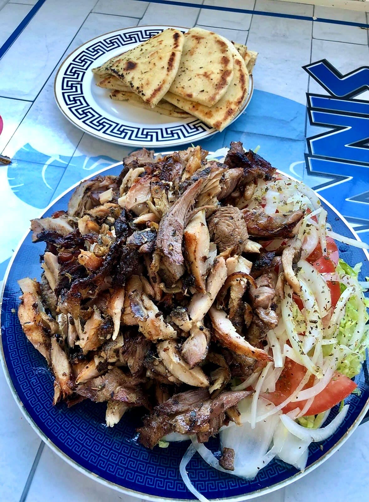 A platter of charcoal meat and salad with pita on a blue Greek-key plate